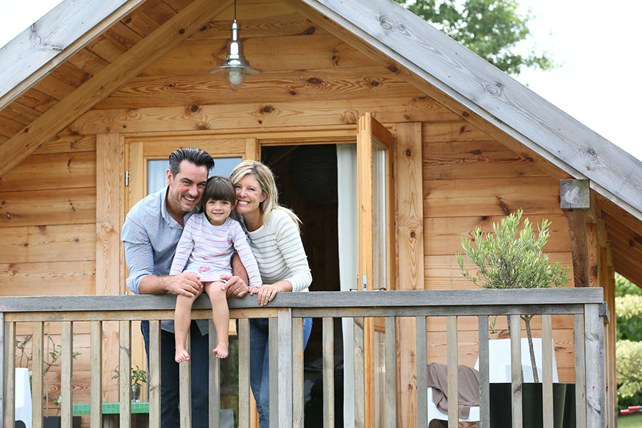 Personal Insurance - Closeup View of Two Smiling Parents and Their Daughter on the Front Balcony of a Wooden Home
